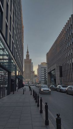 a city street lined with tall buildings and parked cars next to each other on either side of the road