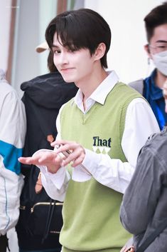 a young man wearing a green sweater and white shirt is standing in front of other people