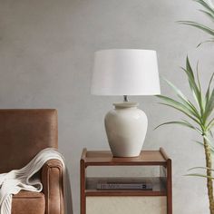 a white lamp sitting on top of a table next to a brown chair and a potted plant