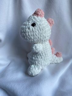 a crocheted white and pink stuffed animal sitting on top of a white sheet