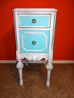 a blue and white nightstand with two drawers on it's sides in front of a red wall