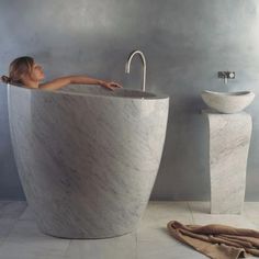 a woman laying in a large bathtub next to a sink and towel on the floor