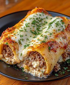 a black plate topped with lasagna covered in cheese and meat sauce on top of a wooden table