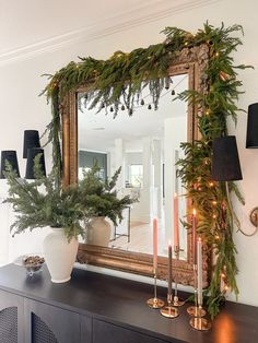 a mirror sitting on top of a dresser next to a christmas wreath and candles in front of it