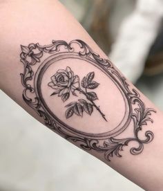 a black and white photo of a rose in a frame on someone's arm