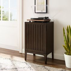 a record player sitting on top of a wooden cabinet next to a potted plant