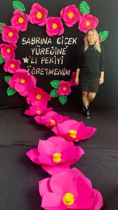 a woman standing in front of a sign with paper flowers on it and the words sabrina cicek yuregine li pekini together