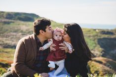 a man, woman and baby are sitting in the grass with mountains in the background