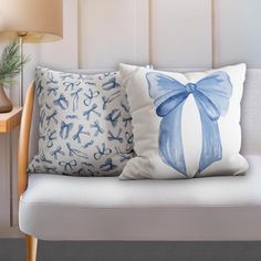 two blue and white pillows sitting on top of a wooden bench next to a lamp