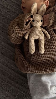 a little boy holding a stuffed animal in his hands and wearing a knitted sweater