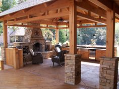 an outdoor kitchen and grill area with wood flooring, stone fireplace and covered patio