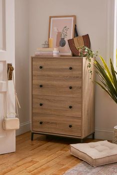 a chest of drawers in the corner of a living room with a plant on top