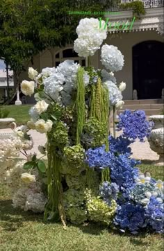 an arrangement of flowers in front of a house on the side of a road with grass and bushes