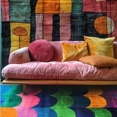 a pink couch with colorful pillows on it in front of a wall hanging from the ceiling