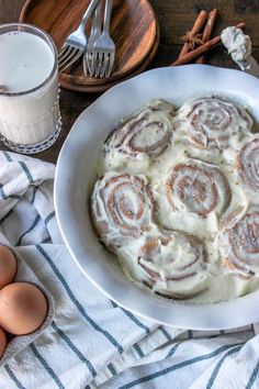 a bowl filled with cinnamon rolls next to some eggs and an empty glass of milk