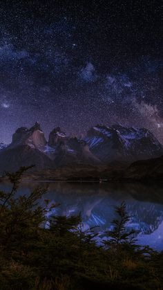 the night sky is filled with stars and clouds above mountains, reflecting in a body of water