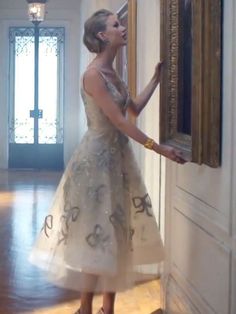 a woman in a white dress is looking at a painting on the wall and holding it up