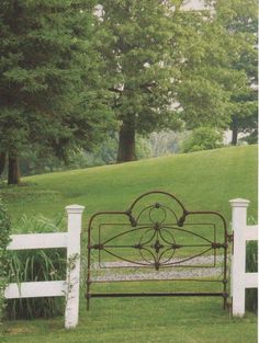 a wrought iron bed frame in the middle of a grassy area near a white picket fence