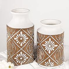 two white vases sitting next to each other on top of a cloth covered table