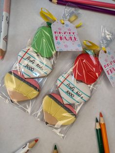 three decorated cookies in plastic wrappers with pencils next to them on a table