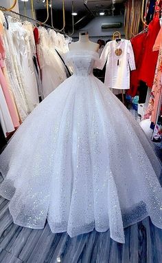 a white wedding dress is on display in a store with clothes hanging up behind it