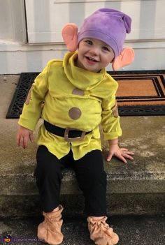 a little boy in a costume sitting on the steps wearing boots and a purple hat