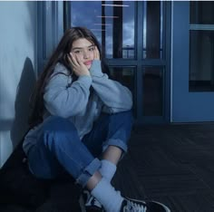 a young woman sitting on the floor with her hand to her face and looking at the camera