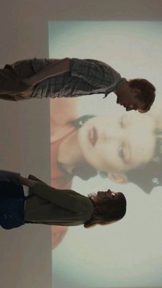 two people standing in front of a large screen with the image of a woman and man on it