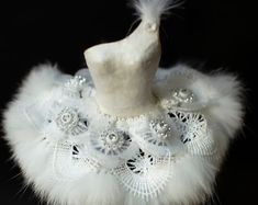 a white mannequin with feathers and lace on it's neck, against a black background