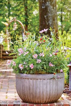 a planter filled with lots of flowers sitting on top of a brick walkway