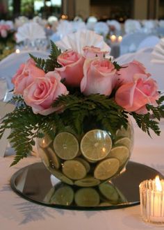 a vase filled with pink roses and lemons on top of a table next to candles