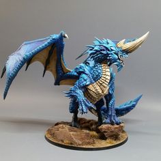 a blue dragon figurine sitting on top of a wooden table next to a gray background