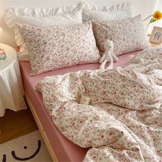 a bed covered in pink and white sheets with flowers on it next to a table