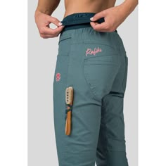 a person holding a brush and toothbrush in their pocket while wearing green pants with pink lettering on the side