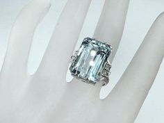 A sizable, frosty pale blue emerald-cut aquamarine shimmers gloriously in its icy white gold and diamond setting in this circa 1940s-50s cocktail ring. Pretty details - diamond-studded crescents abutting rolled shoulders and a fluted gallery - add to the charm and stylish sophistication. The aqua alone measures 18.25mm x 13.0mm x 10.0mm, approx. 19.5ct , diamond approx. 0.24ct, H-I color and VS2-Si1, ring top 20.0mm, ring size 6.75, weight 11.4 grams. Hallmark PT900 Retail $5,500 Rolled Shoulders, Blue Emerald, Aquamarine Engagement Ring, Diamond Settings, Cocktail Ring, Top 20, Cocktail Rings, Rings Statement, Emerald Cut