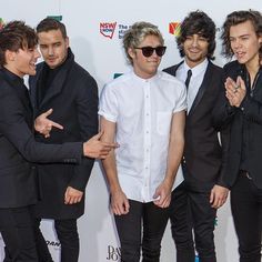 four men in suits and sunglasses posing for a photo on the red carpet at an event