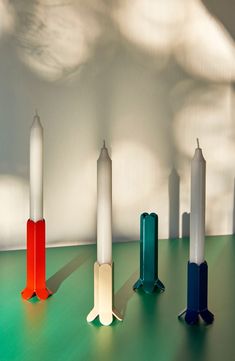 four different colored candles sitting on top of a green table next to a white wall