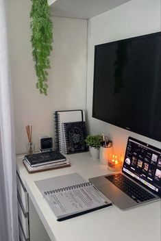 a laptop computer sitting on top of a white desk next to a book and notebook