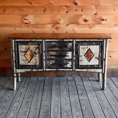 an old dresser is painted black and white with brown diamond designs on the doors, along with wood flooring