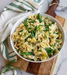 a bowl filled with pasta and vegetables on top of a wooden cutting board next to a towel