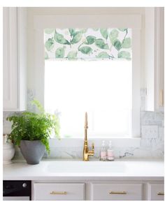 a kitchen sink under a window with green leaves on the valance and gold faucet