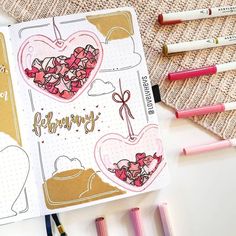 an open notebook with pink and gold hearts on it, surrounded by crayons