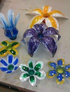 several colorful glass flowers sitting on top of a white table next to another flower vase