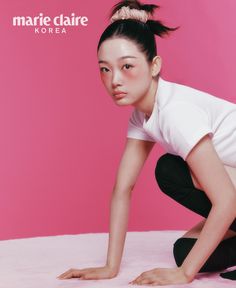 a young woman crouching down in front of a pink background