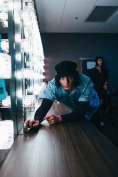 a man leaning over a wooden table in front of a wall with lights on it