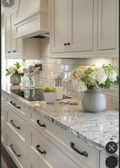 a kitchen with white cabinets and marble counter tops, vases filled with flowers on the island