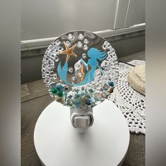 a glass plate with a mermaid on it sitting on top of a white table next to a doily