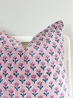 a pink and blue flowered pillow on a white headboard against a white wall