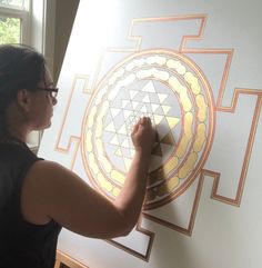 a woman is drawing on a wall with an intricate geometric design in gold and white