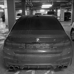 the back end of a car parked in a parking garage next to another car with it's hood up